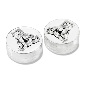 May include: Two silver baby keepsake boxes with a teddy bear design on the lid. The boxes are engraved with the words "Baby" and "First"