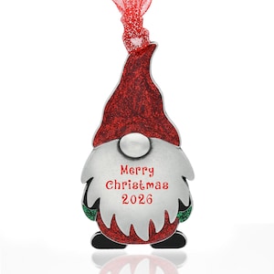 May include: A silver-toned metal gnome ornament featuring a tall, glittery red hat and a long, textured silver beard. The beard is engraved with the red text Merry Christmas 2026. A red ribbon is attached to the top for hanging the ornament.
