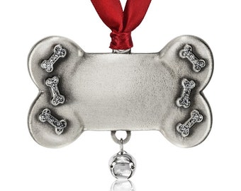 Könnte beinhalten: Ein silberner Knochen-Weihnachtsanhänger mit einem roten Band und einer kleinen Glocke. Der Knochen hat einen leeren Platz zum Personalisieren und ist mit kleinen, glitzernden, weißen Knochen-Akzenten verziert.
