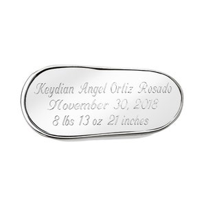 May include: A silver oval-shaped baby keepsake with the inscription "Keydian Angel Ortiz Rosado, November 30, 2018, 8 lbs 13 oz 21 inches".