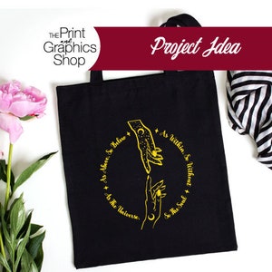 May include: Black tote bag with a gold design featuring two hands reaching towards each other, surrounded by text. The text reads "As Above, So Below, As Within, So Without, As The Universe, So The Soul." The bag has a handle and is on a white surface.
