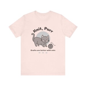 May include: A pink t-shirt with a gray cat illustration and the text "Knit, Purr" and "Crafts are better with cats".