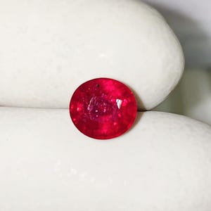 May include: A round, faceted gemstone with a vibrant, deep red colour. The stone displays a polished surface with internal light reflections and a clear, circular cut, showcasing a rich, saturated hue throughout its entire structure.