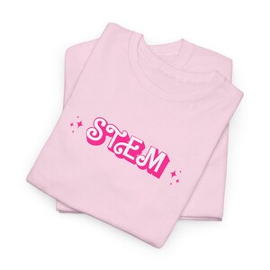 May include: Two light pink t-shirts are stacked, with the top shirt featuring the word "STEM" in a retro, pink and white font. Pink starburst graphics are on either side of the text.