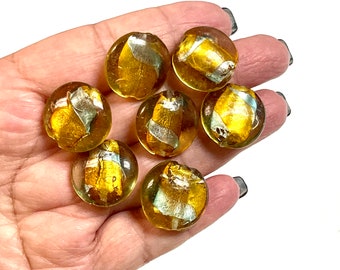 May include: Seven round glass beads with gold and silver foil accents. The beads are translucent and have a slightly iridescent sheen.