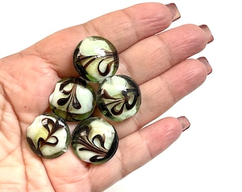 May include: Five round glass beads with a white background and black swirl design. The beads are translucent and have a green tint.
