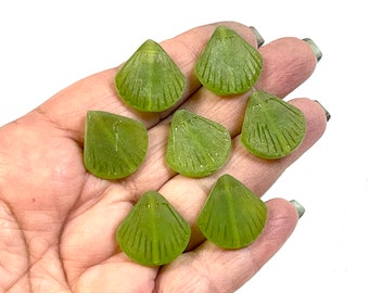 May include: Seven green glass sea shell shaped beads. The beads are translucent and have a slightly frosted finish.