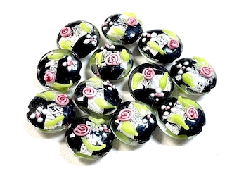 May include: A collection of glass beads with a floral design. Each bead features a black and silver checkered pattern, accented with pink rose-shaped embellishments and light green leaves. The beads are round and have a clear, glossy finish.
