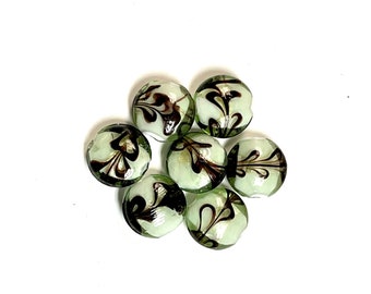 May include: Seven green glass beads with a white swirl and black floral design.