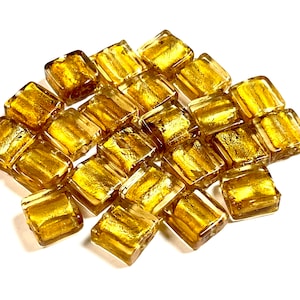 May include: A pile of gold-colored glass tiles with a metallic sheen. The tiles are square and have a slightly irregular shape. They are perfect for adding a touch of sparkle to any craft project.