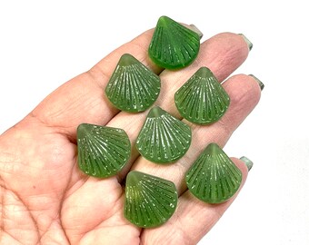 May include: Eight green glass shell-shaped buttons with a raised design. The buttons are arranged in a hand.