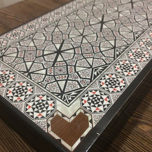 May include: A black wooden box with a geometric pattern inlaid with mother of pearl and red and white accents. The box has a heart-shaped inlay on the front.