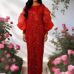 May include: A floor-length red dress featuring a sequined bodice and skirt with long, voluminous sheer organza puff sleeves. The garment has a round neckline and fitted cuffs, paired with matching red open-toe sandals.