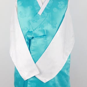 Może przedstawiać: Turkusowy hanbok, tradycyjny koreański strój, z białymi rękawami i granatową wstążką. Hanbok ma kwiatowy wzór.