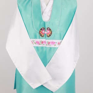 Może przedstawiać: Tradycyjny koreański hanbok w kolorze turkusowym z białymi rękawami i haftowaną wstążką z kwiatami. Hanbok ma ozdobny zapięcie na guziki z kwiatowymi akcentami.