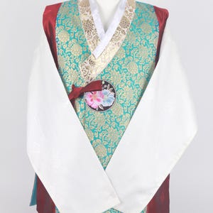 Może przedstawiać: Tradycyjny koreański hanbok, długa szata z długimi rękawami, z gorsetem w kolorze turkusowym i złotym wzorze, białymi rękawami i czerwoną wstążką. Hanbok ma kwiatowy wzór z przodu i turkusową spódnicę.