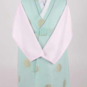 Może przedstawiać: Jas hanbok w jasnym kolorze zielonym z haftowanymi złotymi kółkami, białym kołnierzem i różowymi rękawami. Hanbok jest noszony na czerwonych spodniach.