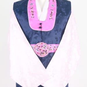 Może przedstawiać: Tradycyjny koreański hanbok, formalny strój, z granatową kurtką i różowymi spodniami. Kurtka ma różowy kołnierz z haftowanymi kwiatami i różową wstążkę z okrągłym wzorem kwiatowym. Rękawy są białe z różowymi lamówkami.
