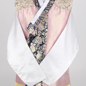 Może przedstawiać: Tradycyjny koreański hanbok, długa koszula z jedwabiu w kolorze różowym i białym. Hanbok zdobi ozdobny pas z kwiatowymi wzorami w kolorze złotym i niebieskim.