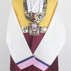 Może przedstawiać: Tradycyjny koreański strój z żółtą górą, bordowym dołem i białymi rękawami z różowymi i niebieskimi lamówkami. Góra ma czarny i złoty wzorzysty kołnierz oraz złoty i bordowy pasek z kwiatowym wzorem.
