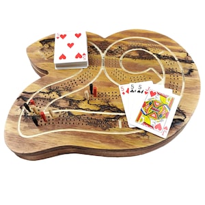 May include: A wooden cribbage board with a unique, organic shape. The board features a brown wood grain with a dark brown stain. The board has a track for pegs and a scoring area. There are playing cards on the board, including a Jack of Hearts, three 5s of Hearts, and a 5 of Hearts.