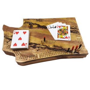 May include: A wooden cribbage board with a unique, natural wood grain pattern. The board is shaped like a state, and there are playing cards and pegs on the board.