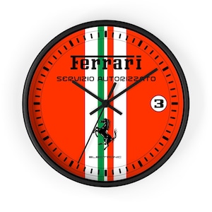 Puede incluir: Reloj de pared redondo con marco negro y esfera roja. La esfera presenta rayas blancas y verdes, el logotipo de Ferrari y un emblema de caballo negro. El reloj tiene manecillas negras y el número 3.
