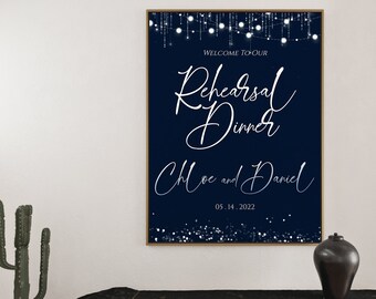 Pode incluir: Uma placa azul marinho com texto branco que diz "Bem-vindos ao nosso jantar de ensaio Chloe e Daniel 05.14.2022". A placa é decorada com luzes de corda brancas e glitter prateado.