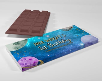 May include: A chocolate bar label with a space theme. The label features a blue galaxy background with planets and the text "PAUL WRIGHT'S 1st Birthday". A brown chocolate bar is next to the label.