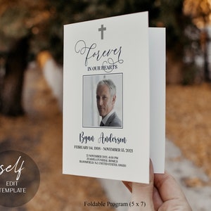 May include: A white folded programme with a black cross at the top and the words "Forever in Our Hearts" in a cursive font. The programme has a photo of a man in a suit and the text "Byan Anderson, February 04, 1998 - November 15, 2021, 21 November 2021, 4:00 PM, Zuasola Funeral Homes, Bloomfield, NJ, United States, 08050". The programme is labelled "Foldable Programme (5 x 7)".