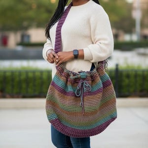May include: A handmade, crochet shoulder bag in a striped pattern of teal, purple, brown, and tan. The bag has a drawstring closure and a wide, solid purple strap. The bag is worn over the shoulder.