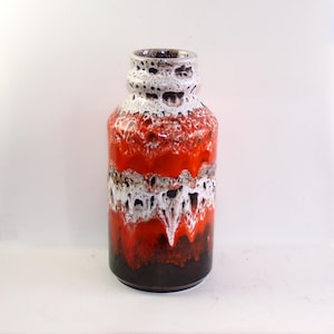 May include: A ceramic vase with a cylindrical body and a textured, layered design. The vase features bands of red, white, and brown colors, with a dark brown base and a white and brown speckled rim. The vase is approximately 10 inches tall.