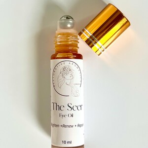 May include: A gold and silver roller bottle with a label that reads "The Seer Eye Oil Brighten + Renew + Repair 10 ml".