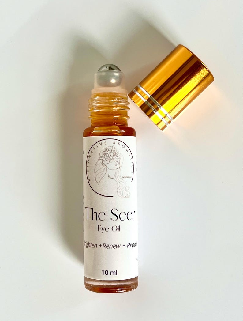 May include: A gold and silver roller bottle with a label that reads "The Seer Eye Oil Brighten + Renew + Repair 10 ml".