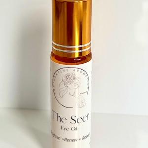 May include: A gold and white roll-on bottle with a label that reads "The Seer Eye Oil" and "Brighten + Renew + Repair". The bottle contains 10 ml of oil.