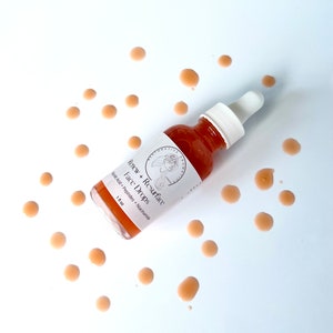 Może przedstawiać: Przezroczysta szklana butelka z kroplomierzem wypełniona jasno pomarańczowym płynem. Butelka jest oznaczona etykietą "Renew + Resurface Face Drops Hyaluronic Acid + Peptides + Niacinamide 1 fl oz". Butelka jest otoczona małymi, jasno pomarańczowymi kroplami na białym tle.