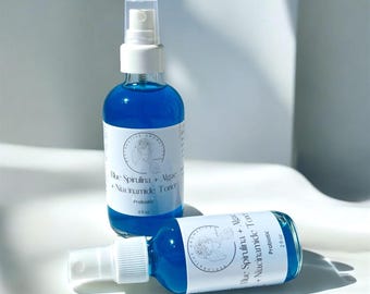 Könnte beinhalten: Zwei blaue Glasflaschen mit weißen Sprühköpfen und Etiketten. Die Etiketten haben einen weißen Hintergrund mit schwarzem Text, der "Blue Spirulina + Algae + Niacinamide Toner" und "Probiotic" lautet. Die Flasche links ist 4 fl oz und die Flasche rechts ist 2 fl oz.