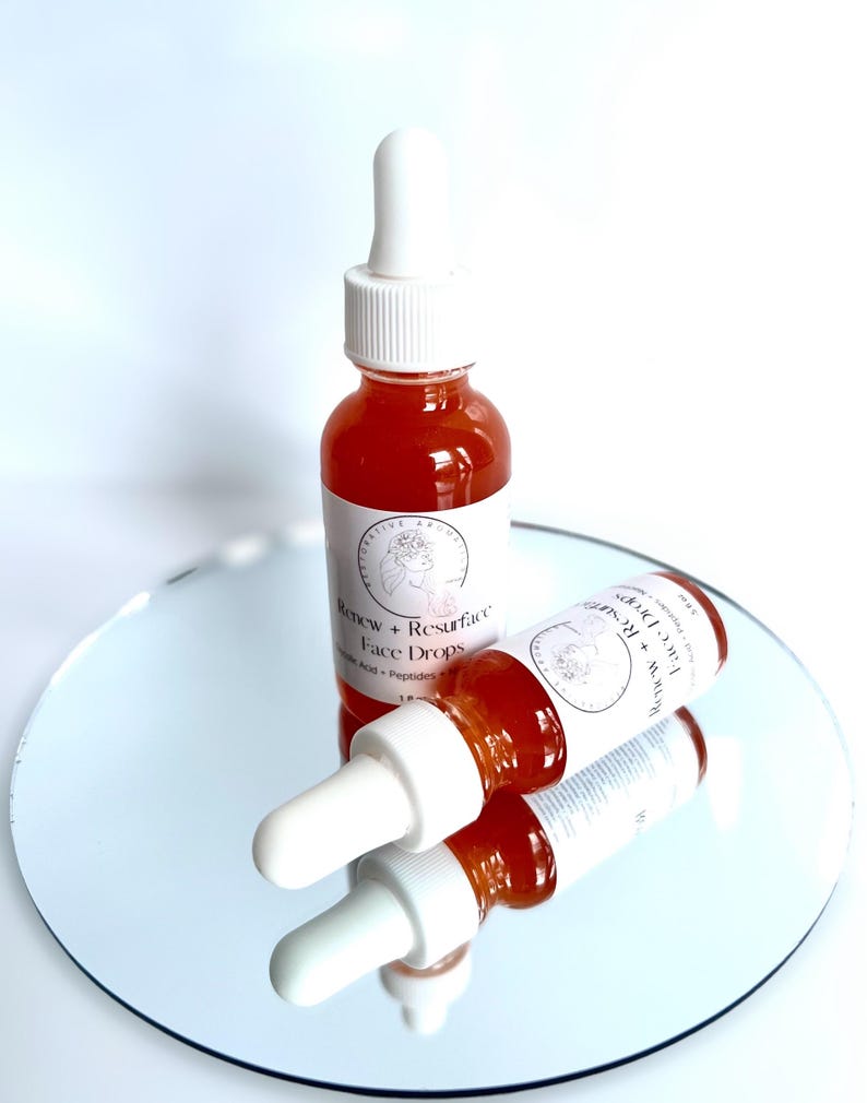 Może przedstawiać: Dwie bursztynowe butelki ze szklanymi pipetkami wypełnione jasnopomarańczowym płynem. Butelki są oznaczone etykietą "Renew + Resurface Face Drops".