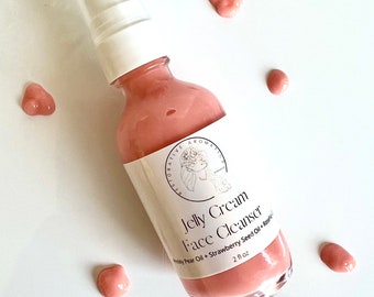 May include: A clear glass bottle with a white pump top filled with a pink jelly cream cleanser. The bottle has a white label with the text "Jelly Cream Face Cleanser Prickly Pear Oil + Strawberry Seed Oil + Raspberry" and "2 fl oz".