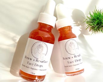 Könnte beinhalten: Zwei bernsteinfarbene Glasflaschen mit weißen Tropfern und weißen Etiketten. Die Etiketten haben ein florales Design und den Text "Renew + Resurface Face Drops". Die kleinere Flasche trägt die Aufschrift "5 fl oz" und die größere "1 fl oz".