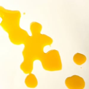May include: A yellow liquid has been spilled on a white surface, creating an abstract shape with several smaller droplets.