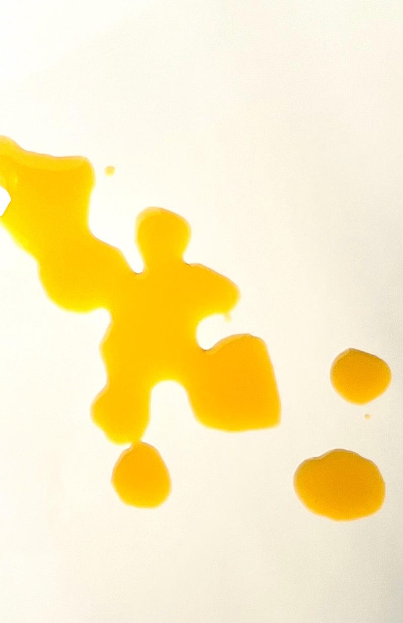 May include: A yellow liquid has been spilled on a white surface, creating an abstract shape with several smaller droplets.