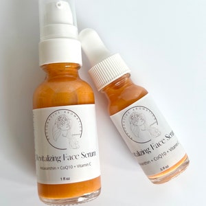 May include: Two amber glass bottles with dropper tops and labels. The larger bottle is labeled "Revitalizing Face Serum Astaxanthin + CoQ10 + Vitamin C 1 fl oz". The smaller bottle is labeled "Vitalizing Face Serum Astaxanthin + CoQ10 + Vitamin C 5 fl oz".