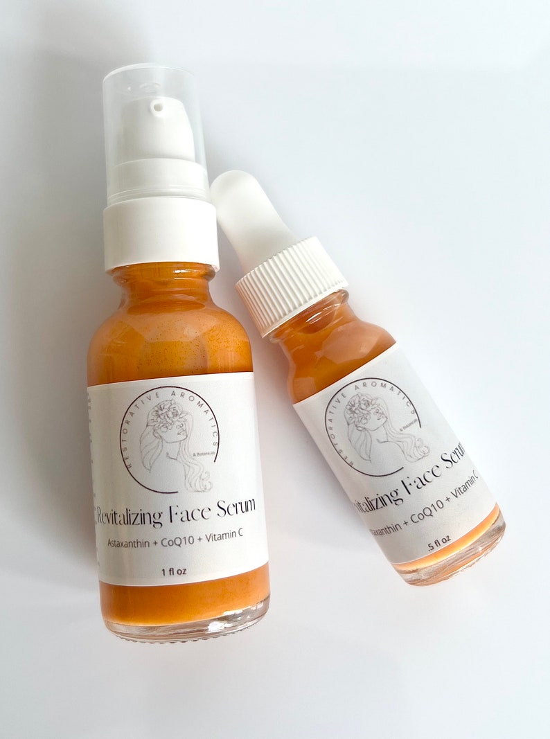 May include: Two amber glass bottles with dropper tops and labels. The larger bottle is labeled "Revitalizing Face Serum Astaxanthin + CoQ10 + Vitamin C 1 fl oz". The smaller bottle is labeled "Vitalizing Face Serum Astaxanthin + CoQ10 + Vitamin C 5 fl oz".
