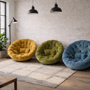 May include: Three tufted, round accent chairs in mustard yellow, olive green, and blue. Each chair has a matching small pillow. The chairs are on a patterned rug in a room with a brick wall and large window.