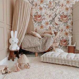 May include: A child's bedroom with floral wallpaper and a patterned rug. Includes a white bunny lamp, a wicker chair, and a floor cushion. The room is decorated in soft, neutral tones, creating a warm and inviting atmosphere.