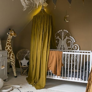 May include: A child's bedroom with a white cot, a giraffe toy, and a woven rug with a black geometric pattern. A mustard-coloured canopy hangs over the cot, and a star-shaped pillow sits on a wicker chair.