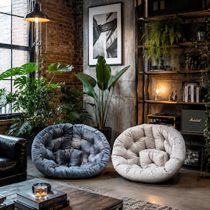 May include: Two round, tufted lounge chairs with plush, velvet-like upholstery. One chair is dark blue and the other is light beige. Each chair features a circular, button-tufted design with a matching small, square-shaped cushion in the center.