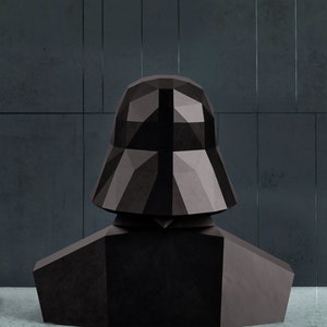 Puede incluir: Un busto geom&eacute;trico negro de Darth Vader, con un casco y hombros detallados. La escultura est&aacute; hecha de material oscuro y texturizado, con un dise&ntilde;o facetado. El fondo es una pared gris oscuro.
