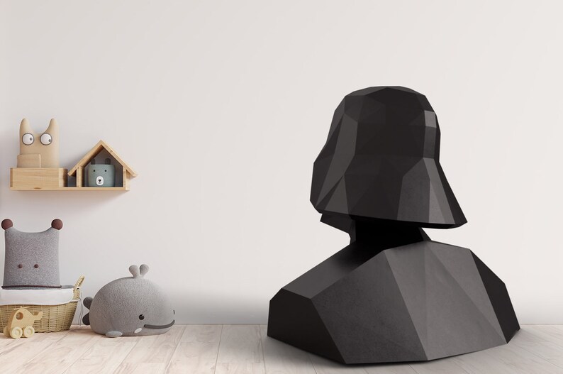 Puede incluir: Un busto negro y geom&eacute;trico de Darth Vader, un personaje de Star Wars, est&aacute; sobre un suelo de madera. El busto est&aacute; hecho de planos angulares y planos. Una estanter&iacute;a con objetos decorativos est&aacute; en el fondo.